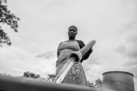 Téléchargez les photos : Abuja, Nigéria - 8 octobre 2022 : Femme africaine qui va chercher de l'eau. Clean Water Solution in African Community ". Happy African Récupération d'eau dans un seau - en image libre de droit