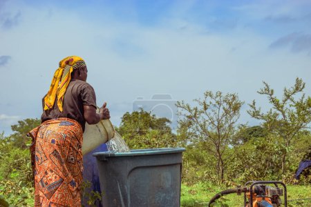 Téléchargez les photos : Abuja, Nigéria - 8 octobre 2022 : Des Africains vont chercher de l'eau. Clean Water Solution in African Community ". Happy African Récupération d'eau dans un seau. - en image libre de droit