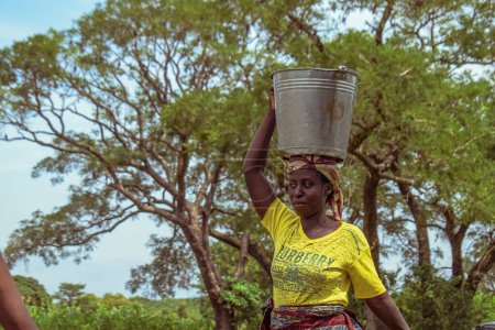 Foto de Abuja, Nigeria - 8 de octubre de 2022: Mujer africana con cubo de agua. Solución de Agua Limpia en Comunidad Africana. Feliz africano fetching agua en un cubo. - Imagen libre de derechos