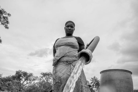 Foto de Abuja, Nigeria - 8 de octubre de 2022: Mujer africana Fetching Water. Solución de Agua Limpia en Comunidad Africana. Feliz africano fetching agua en un cubo - Imagen libre de derechos