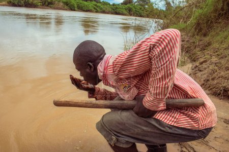 Téléchargez les photos : Delta State, Nigeria - 9 décembre 2021 : Homme africain buvant de l'eau de rivière, Nigeria - en image libre de droit
