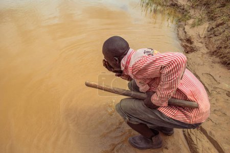 Photo for Delta State, Nigeria - December 9, 2021: African man drinking water from river, Nigeria - Royalty Free Image
