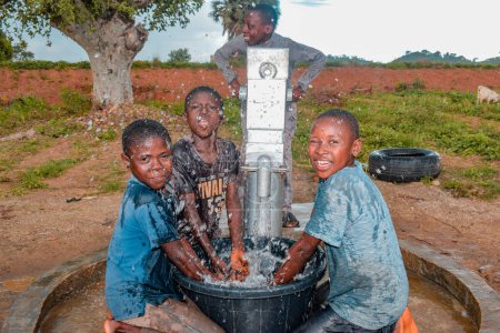 Téléchargez les photos : Abuja, Nigeria - Le 02 août 2021 : Les enfants africains s'amusent en exprimant bonheur et rire tout en jouant avec de l'eau propre sous le soleil dans une communauté rurale. Enfants joyeux et reconnaissants - en image libre de droit