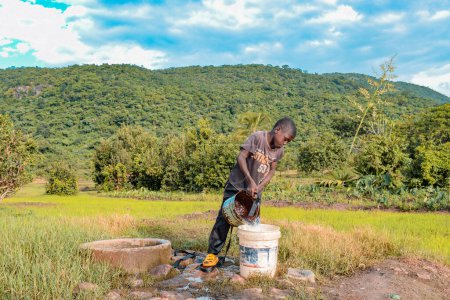 Foto de Nigeria - 20 de junio de 2023: Niño africano vertiendo agua de un cubo a otro. Problema de agua - Imagen libre de derechos
