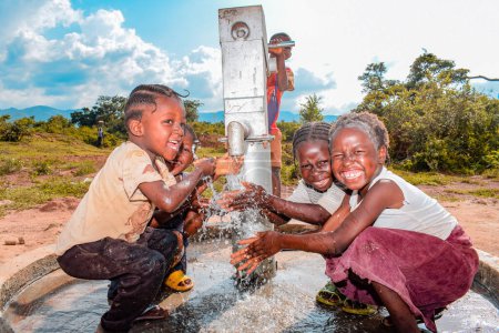 Foto de Abuja, Nigeria - 02 de agosto de 2021: Niños africanos se divierten mientras expresan felicidad y risa mientras juegan con agua limpia bajo el sol en una comunidad rural. Niños alegres y agradecidos - Imagen libre de derechos
