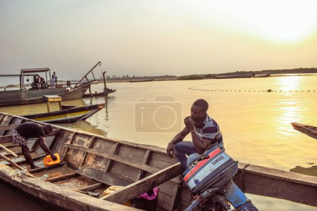 Téléchargez les photos : Delta State, Nigeria - 9 décembre 2021 : Canoës fabriqués localement au bord d'une rivière sur le fleuve Niger compensant un magnifique lever de soleil. Bateaux de pêche au bord d'une rivière. Réflexion sur une surface d'eau. - en image libre de droit