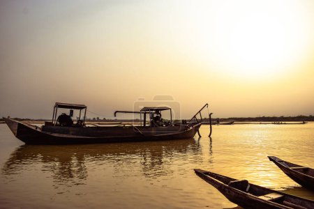 Foto de Estado del Delta, Nigeria - 9 de diciembre de 2021: Canoas hechas localmente junto a un río en el río Níger compensando un hermoso amanecer. Barcos de pesca en la orilla de un río. Reflexión sobre una superficie de agua. - Imagen libre de derechos