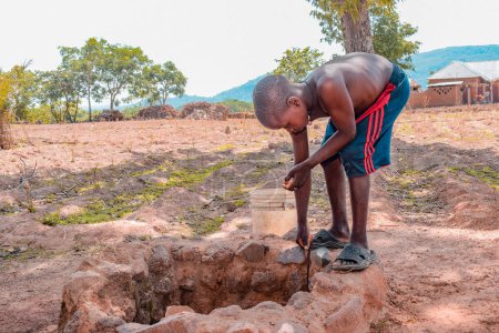 Téléchargez les photos : Jos East, État du Plateau - 12 mai 2021 : Un adolescent africain récupère de l'eau d'un puits creusé à la main dans une communauté rurale. Eau boueuse brute non traitée - en image libre de droit