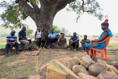 Téléchargez les photos : Nigeria - 20 juin 2023 : Des hommes africains parlent en plein air assis en cercle sous un grand arbre - en image libre de droit