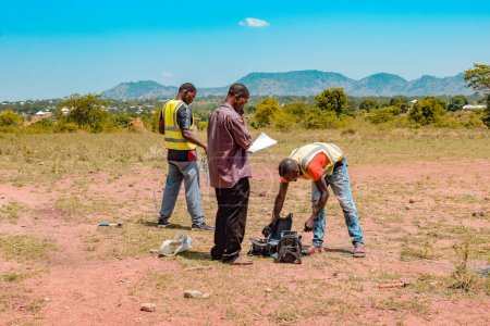 Foto de Jos East, Plateau State - 12 de mayo de 2021: Geólogo africano y miembros del equipo que realizan una encuesta geofísica sobre la disponibilidad del agua en el suelo. Ciencias del Suelo. Proyecto Agua Rural. - Imagen libre de derechos