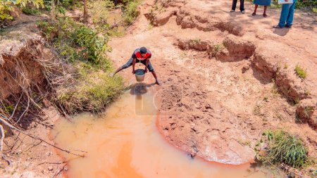 Foto de Jos East, Plateau State - 12 de mayo de 2021: El hombre africano captura agua contaminada e inmunda de un estanque o arroyo para su consumo diario - Imagen libre de derechos