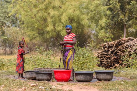 Foto de Abaji, FCT Abuja - 20 de enero de 2023: Una mujer africana extrae agua de un pozo abierto excavado a mano en una comunidad rural. - Imagen libre de derechos