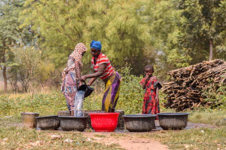 Foto de Abaji, FCT Abuja - 20 de enero de 2023: Una mujer africana extrae agua de un pozo abierto excavado a mano en una comunidad rural. - Imagen libre de derechos