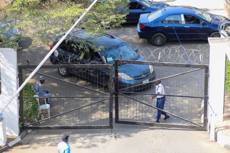 Foto de Abaji, FCT Abuja - 20 de enero de 2023: El hombre de seguridad en uniforme abre la puerta de entrada a un complejo de oficinas. Entrada de aparcamiento - Imagen libre de derechos