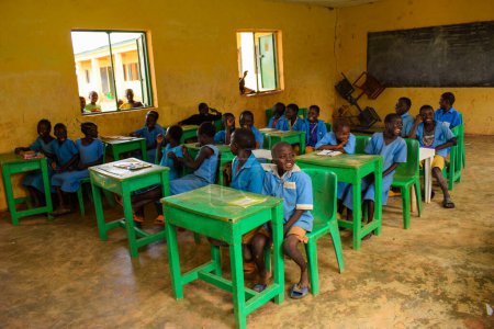 Foto de Abuja, Nigeria - 6 de junio de 2022: Retrato de un niño africano aprendiendo en una comunidad rural. Niños africanos sonrientes vistiendo uniforme escolar en un aula. Educación primaria en aldeas africanas. - Imagen libre de derechos