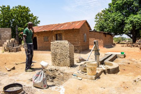Foto de Karara, Nasarawa State - 5 de mayo de 2021: El hombre africano construye una estación de perforación de bombas de mano bajo el sol en una comunidad rural - Imagen libre de derechos