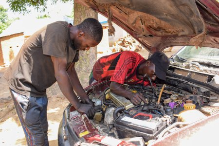 Foto de Karara, Nasarawa State - 5 de mayo de 2021: El mecánico africano arregla un automóvil averiado en una comunidad rural con su amigo - Imagen libre de derechos