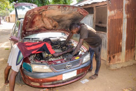 Foto de Karara, Nasarawa State - 5 de mayo de 2021: El mecánico africano arregla un automóvil averiado en una comunidad rural con su amigo - Imagen libre de derechos