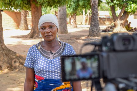 Foto de Karara, Nasarawa State - 5 de mayo de 2021: Madre africana de pie ante una cámara está siendo entrevistada para un equipo de medios de comunicación en su aldea. - Imagen libre de derechos