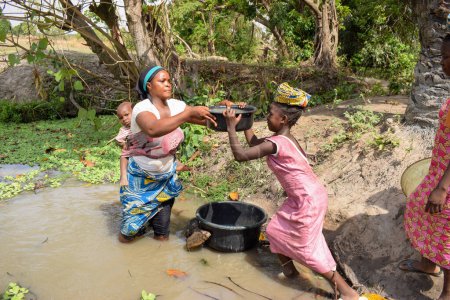 Téléchargez les photos : Karara, État de Nasarawa - 5 mai 2021 : Une femme africaine avec son bébé récupère de l'eau impure et contaminée d'un étang ou d'un ruisseau pour sa consommation quotidienne - en image libre de droit