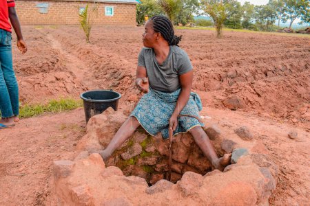 Téléchargez les photos : Jos East, État du Plateau - 12 septembre 2021 : Une adolescente africaine récupère l'eau d'un puits creusé à la main dans une communauté rurale. Eau boueuse brute non traitée - en image libre de droit