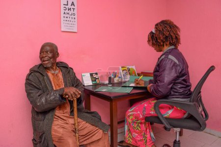 Photo for Abuja, Nigeria - August 09, 2021: Middle Aged African Visits Medical Doctor for Eye Consultation in Rural clinic. Eye Checkup and Eye Test - Royalty Free Image
