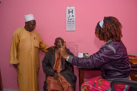 Foto de Abuja, Nigeria - 09 de agosto de 2021: Visita al médico africano de mediana edad para la consulta ocular en una clínica rural. Chequeo ocular y prueba ocular - Imagen libre de derechos