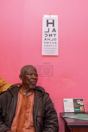 Photo for Abuja, Nigeria - August 09, 2021: Middle Aged African Visits Medical Doctor for Eye Consultation in Rural clinic. Eye Checkup and Eye Test - Royalty Free Image
