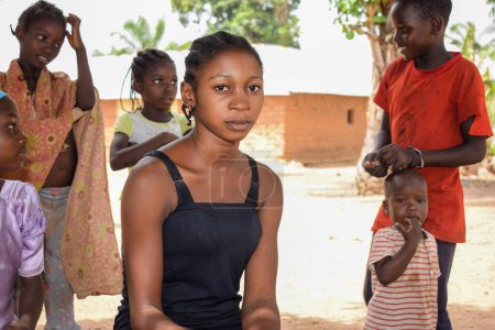 Foto de Karara, Nasarawa State - 5 de mayo de 2021: Adolescente africana mira a la cámara mientras agrieta la cáscara de cacahuete en una comunidad rural - Imagen libre de derechos