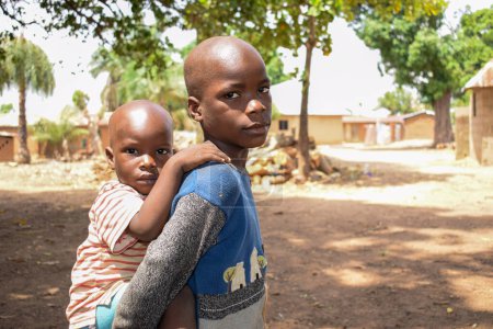 Téléchargez les photos : Karara, État de Nasarawa - 5 mai 2021 : Portrait d'un enfant africain portant son frère sur le dos - en image libre de droit