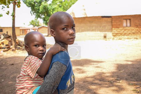 Photo for Karara, Nasarawa State - May 5, 2021: Portrait of an African Male Child Carrying his Sibling on the back - Royalty Free Image