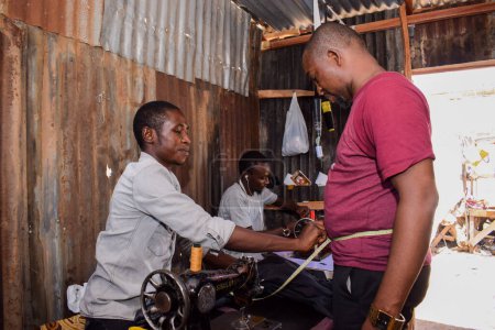 Téléchargez les photos : Jos, Etat du Plateau - 21 avril 2021 : African Tailor working with client at workshop - en image libre de droit