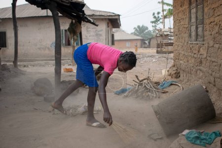 Photo for Opialu, Benue State - March 6, 2021: African Lady Sweeping in a Rural Environment - Royalty Free Image