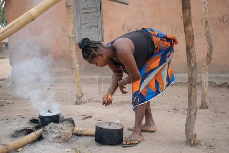 Photo for Opialu, Benue State - March 6, 2021: Mature African Woman Cooking Outdoor with a Firewood - Royalty Free Image