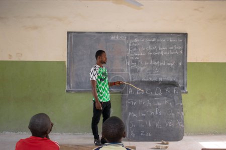 Téléchargez les photos : Opialu, État de Benue, Nigéria - 6 mars 2021 : Un enseignant africain enseigne l'anglais à ses élèves dans une communauté rurale - en image libre de droit