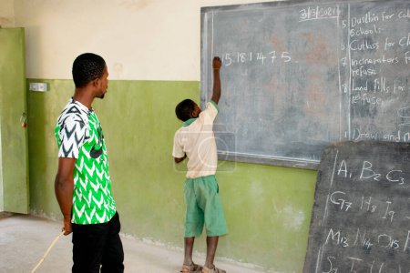 Téléchargez les photos : Opialu, État de Benue, Nigéria - 6 mars 2021 : Un enseignant africain enseigne l'anglais à ses élèves dans une communauté rurale - en image libre de droit