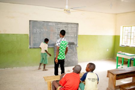 Photo for Opialu, Benue State, Nigeria - March 6, 2021: African teacher teaching his students english language in a rural community - Royalty Free Image