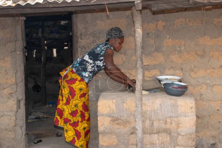 Téléchargez les photos : Opialu, État de Benue - Mars 6, 2021 : Femme africaine utilisant ses mains sur un broyeur local (pierre) pour écraser Melon près de sa maison de boue. - en image libre de droit