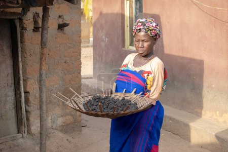 Photo for Opialu, Benue State - March 6, 2021: Middle-Aged African Woman going about her Morning Chores - Royalty Free Image