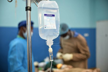 Téléchargez les photos : Abuja Nigeria - July 7, 2023: African Plastic Surgeons in a soft focus blue background. Normal Saline IV infusion prepared for surgery. - en image libre de droit