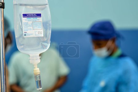 Foto de Abuja Nigeria - July 7, 2023: African Plastic Surgeons in a soft focus blue background. Normal Saline IV infusion prepared for surgery. - Imagen libre de derechos