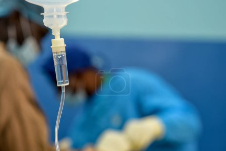 Photo for Abuja Nigeria - July 7, 2023: African Plastic Surgeons in a soft focus blue background. Normal Saline IV infusion prepared for surgery. - Royalty Free Image
