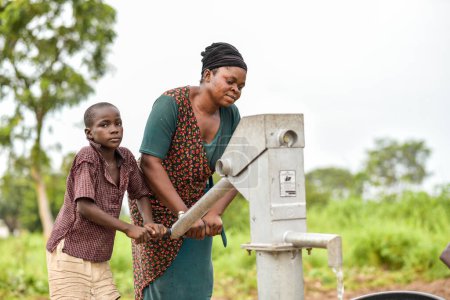 Foto de Talata, Plateau State - 2 de abril de 2023: Mujer y niño africanos indígenas que buscan agua de una bomba de mano india recién construida. Miembros de la comunidad que buscan agua para uso doméstico. - Imagen libre de derechos