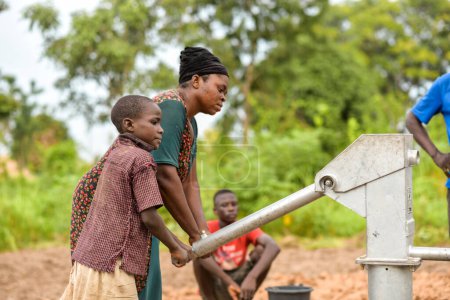 Foto de Talata, Plateau State - 2 de abril de 2023: Mujer y niño africanos indígenas que buscan agua de una bomba de mano india recién construida. Miembros de la comunidad que buscan agua para uso doméstico. - Imagen libre de derechos