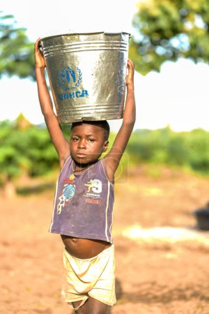 Téléchargez les photos : Talata, État du Plateau - Juin, 2023 : Garçon africain transportant l'eau d'une pompe à main indienne nouvellement construite. Les membres de la communauté vont chercher de l'eau pour usage domestique. - en image libre de droit