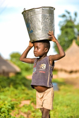 Téléchargez les photos : Talata, État du Plateau - Juin, 2023 : Garçon africain transportant l'eau d'une pompe à main indienne nouvellement construite. Les membres de la communauté vont chercher de l'eau pour usage domestique. - en image libre de droit