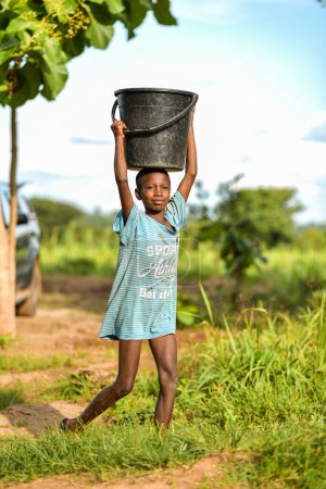 Foto de Talata, Plateau State - June, 2023: African Boy carrying Water from a Newly Built Indian Hand Pump. Miembros de la comunidad que buscan agua para uso doméstico. - Imagen libre de derechos