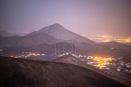 Téléchargez les photos : Arrecife la nuit vu du haut d'un volcan sur lanzarote. Le ciel est violet et vous pouvez voir l'aéroport de Lanzarote en arrière-plan - en image libre de droit