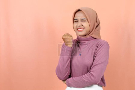 Photo for Excited young Asian woman with clenched fists and raised hands wearing a purple sweater isolated peach background - Royalty Free Image