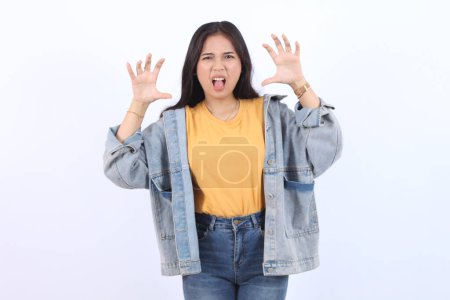 Joven hermosa mujer asiática con chaqueta azul camiseta amarilla boca abierta rugido haciendo gesto de garra como gato, expresión agresiva y sexy
